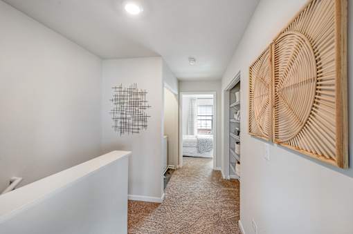 A hallway with a white wall and a wooden artwork on the right side.