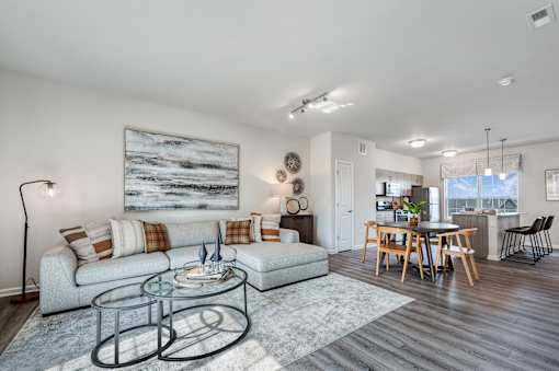 A modern living room with a grey sofa, a glass coffee table, and a large painting on the wall.