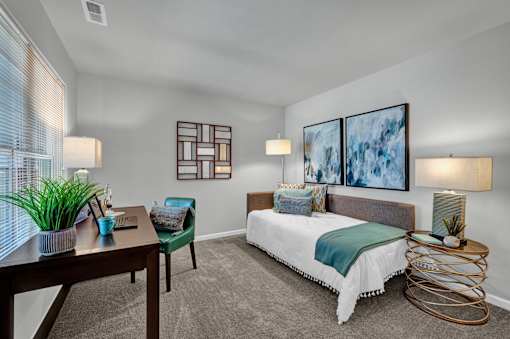 A bedroom with a bed, a chair, a table, and a painting on the wall.