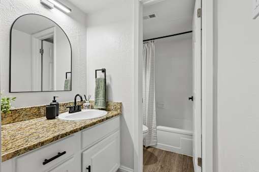 A bathroom with a sink, mirror, and shower.