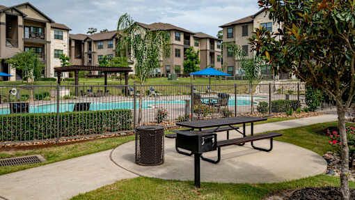 A park area with a picnic table and a trash can in front of apartment buildings.