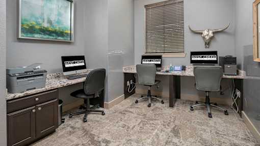 A room with a desk, chairs, and a painting on the wall.
