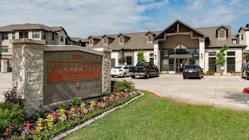 The image shows the entrance to West Creek Apartments with a sign and a flower bed in the foreground.