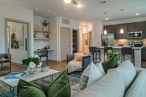 a living room with a couch and a coffee table in front of a kitchen with a counter