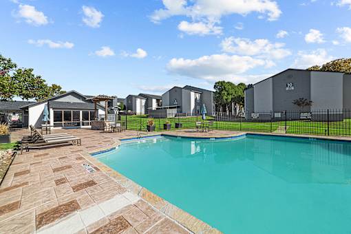 A swimming pool surrounded by a brick patio and a black fence.