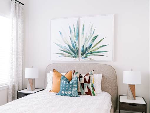 A bedroom with a bed, two lamps, and a painting of a plant.