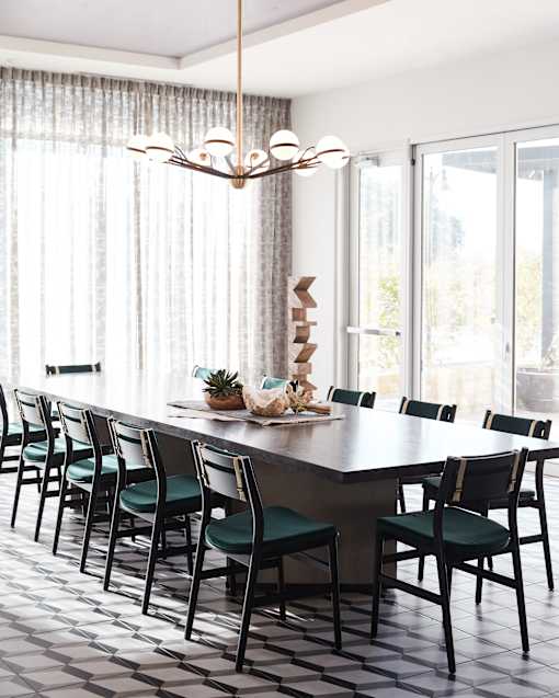 A long dining table with chairs and a chandelier in a room.