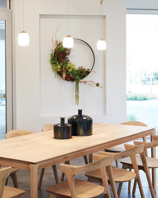 A dining table with chairs and a wreath on the wall.