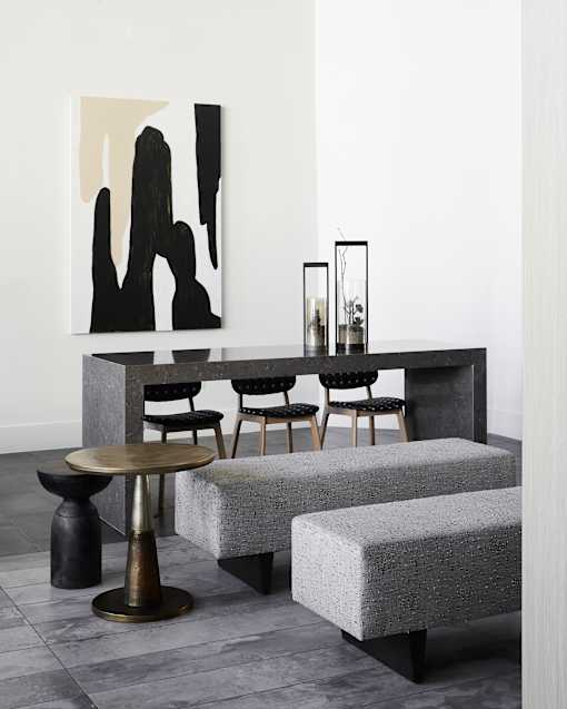 A black and white painting hangs on a white wall above a black table with a glass vase on it.