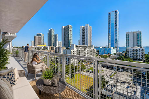 A woman is sitting on a balcony with a view of a city skyline.