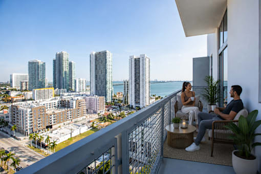 Two people sitting on a balcony overlooking a cityscape.