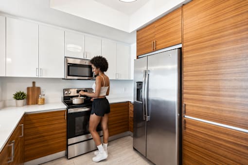 A woman is standing in a kitchen with a stove and refrigerator.