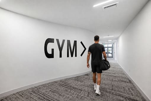 A man walking in a hallway with a Gym sign on the wall.