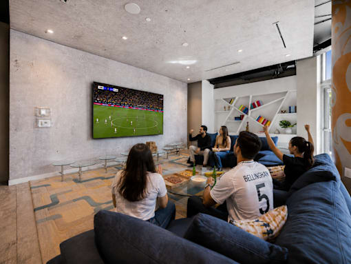 A group of people are watching a soccer game on a large TV screen in a modern living room.