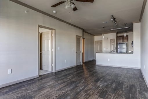 an empty living room with a ceiling fan and a kitchen in the background