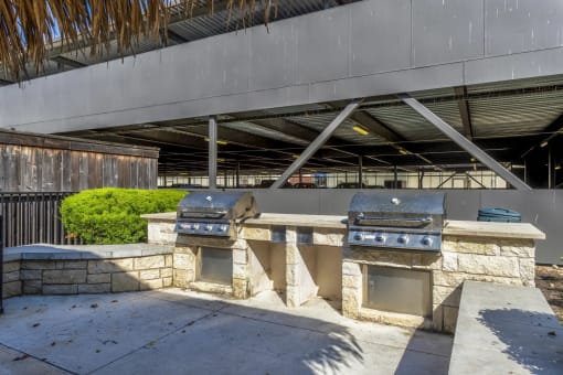 an outdoor kitchen with two bbq grills in front of a building