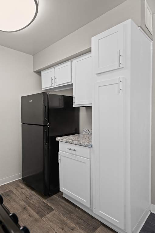 A black refrigerator is in a kitchen with white cabinets.