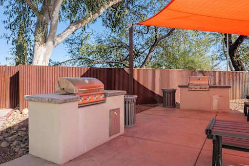 A patio with a grill and an orange umbrella.