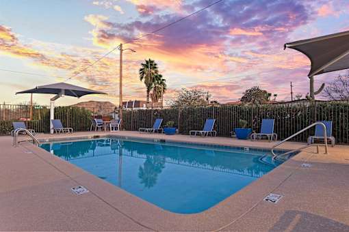 A pool surrounded by chairs and a fence with a sunset in the background.