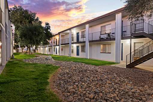 A sunset view of apartment buildings with balconies and a gravel path.
