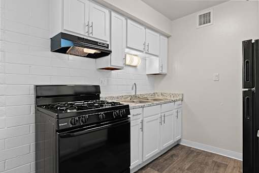 A black stove in a kitchen with white cabinets and a marble countertop.