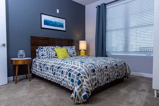 A bedroom with a bed, nightstand, and a painting on the wall.