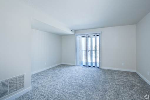 A room with a carpeted floor and a window with blinds.