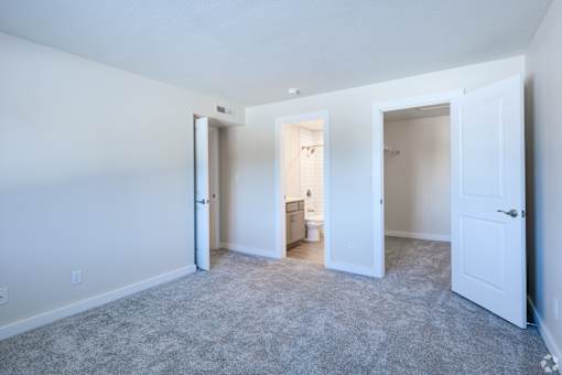 A room with carpeted floor and white walls with three doors.