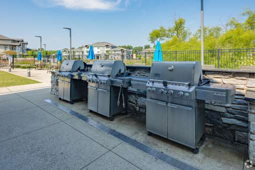 A set of four outdoor grills are lined up on a patio.