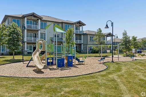 A playground with a slide and a green play structure in front of apartment buildings.