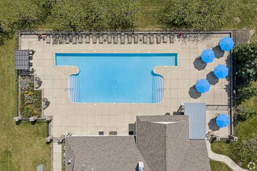 A large swimming pool surrounded by a concrete patio and blue umbrellas.