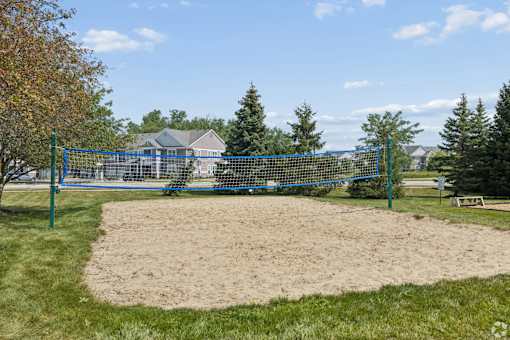 A sandy area with a blue fence and trees in the background.