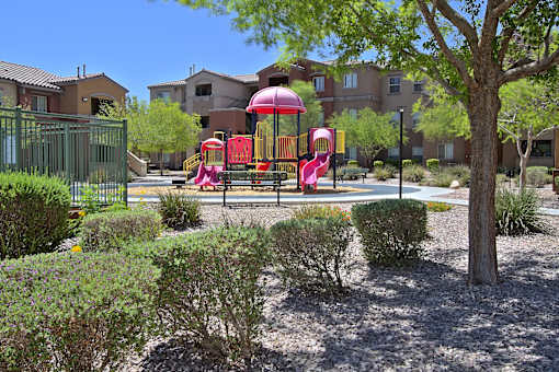 A playground with a red slide and a tree in the foreground.