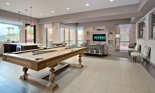 A pool table is in the middle of a room with a TV and a chair.