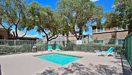 A pool surrounded by trees and chairs.