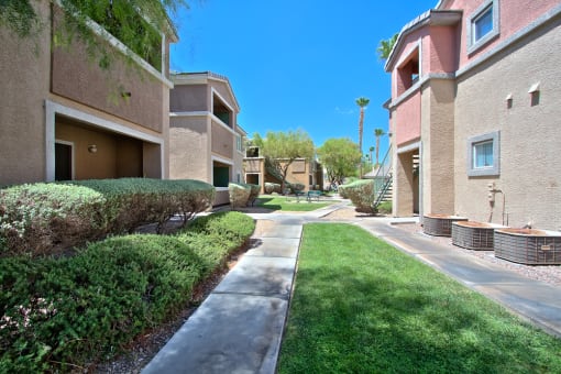 a sidewalk between two apartment buildings with grass and bushes