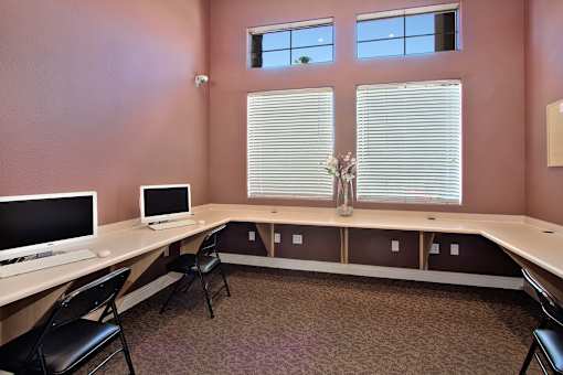 A room with a desk, chairs, and two monitors.