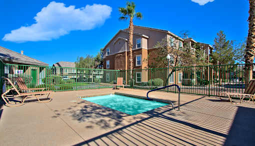 A pool surrounded by a fence and chairs in front of a building.