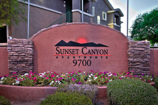 a sign for sunset canyon apartments in front of flowers