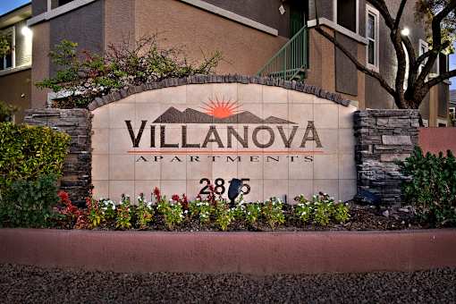 A sign for Villanova Apartments is surrounded by plants and flowers.