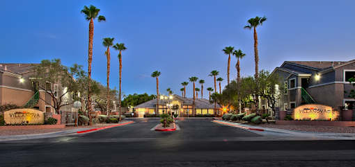 A street view of a residential area with palm trees and a sign that reads "Villagio.".