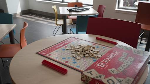 A Scrabble board game is set up on a table in a room with chairs at Denver Metro Village Apartments, Colorado