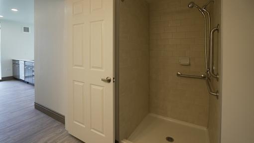 A white door is open to a bathroom with a walk-in shower at Denver Metro Village Apartments, Denver, 80204