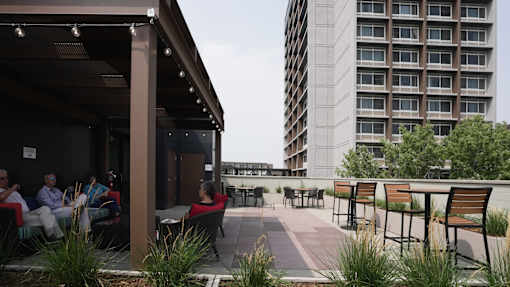 A group of people are sitting on a patio with a building in the background at Denver Metro Village Apartments, Denver, Colorado