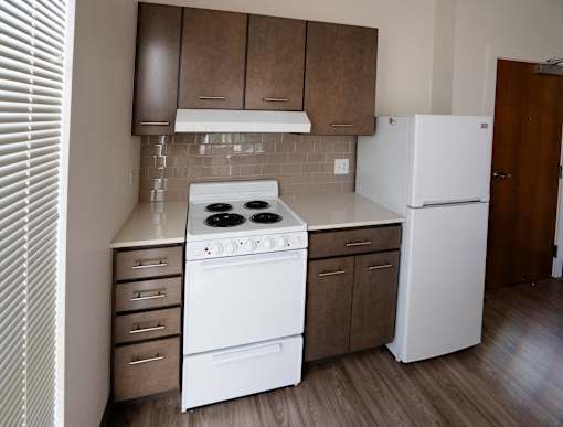 A white stove and refrigerator in a kitchen with brown cabinets at Denver Metro Village Apartments, Colorado