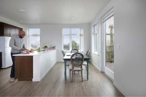 A man is preparing food in a modern kitchen with a dining table and chairs.