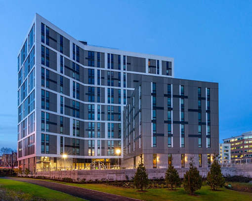 A modern building with a curved facade and multiple windows is illuminated from within.