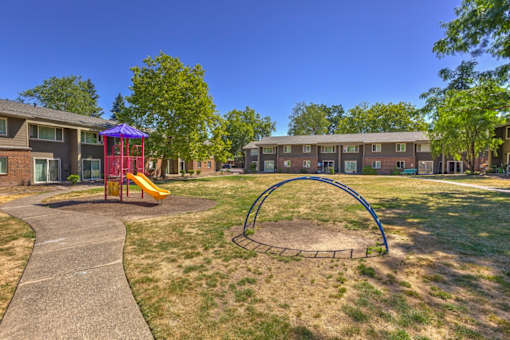 A playground with a slide and a roundabout in front of apartment buildings.
