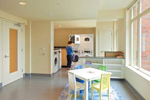 A woman is standing in a kitchen with a washing machine.