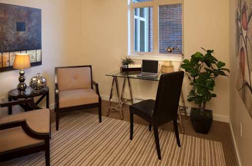 A room with a desk, chair, and potted plant.